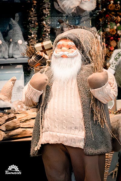 Père Noël de la fôret en pull blanc gilet vert avec un fagot de bois sur le dos
